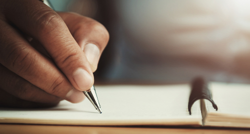 hand of woman holding pen with writing on notebook in office - IACBE